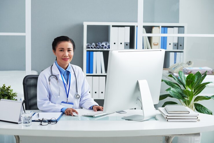 portrait-smiling-general-practitioner-labcoat-working-computer-her-office-desk_274689-27208